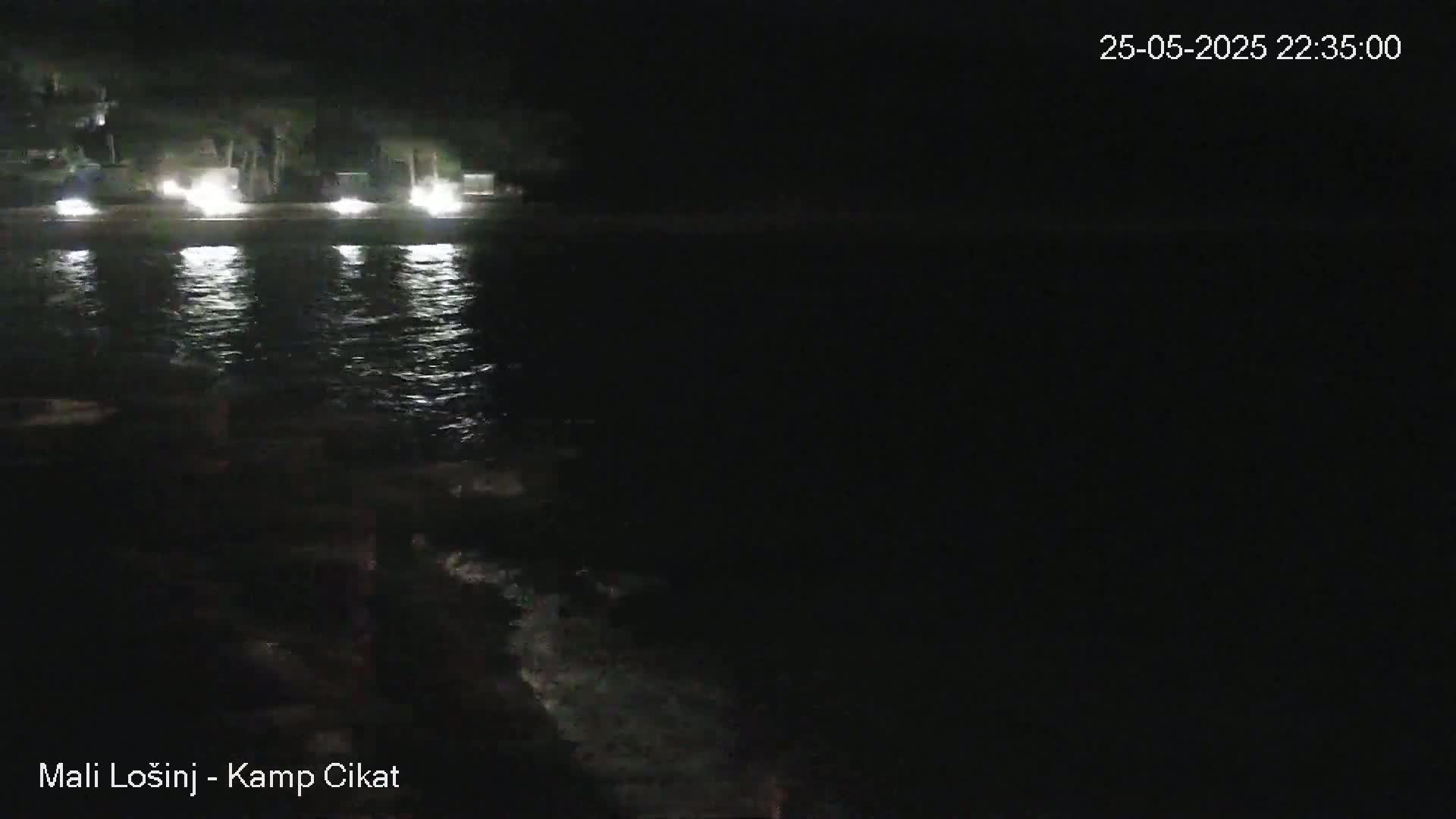 A nighttime view of calm water reflecting lights from a shoreline.