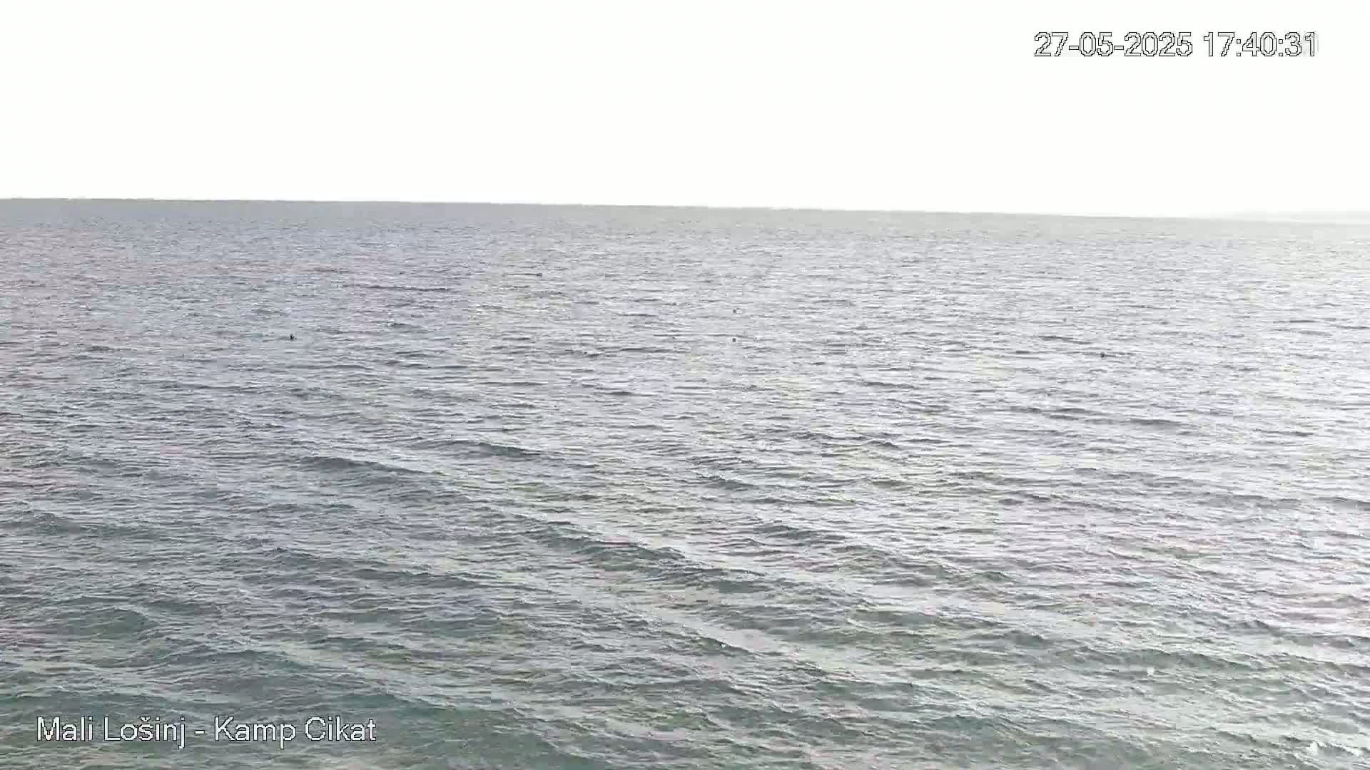 A calm sea with small waves under a bright, overcast sky.