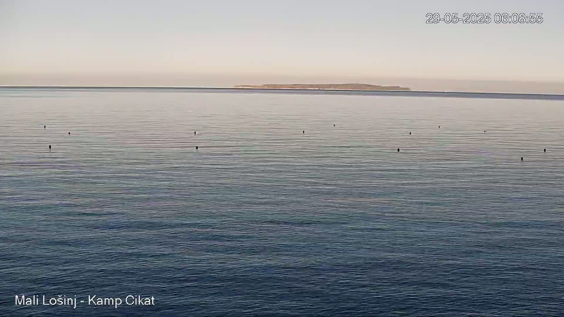 A calm, light-grey ocean with several dark buoys and a distant island under a pale sky.