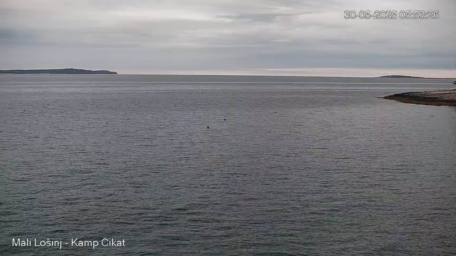 A calm, overcast day shows a wide expanse of dark-grey water with distant islands under a cloudy sky.