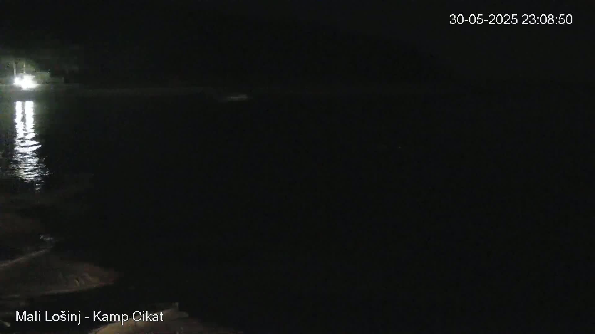 A nighttime view shows a dark body of water reflecting lights from the shore.