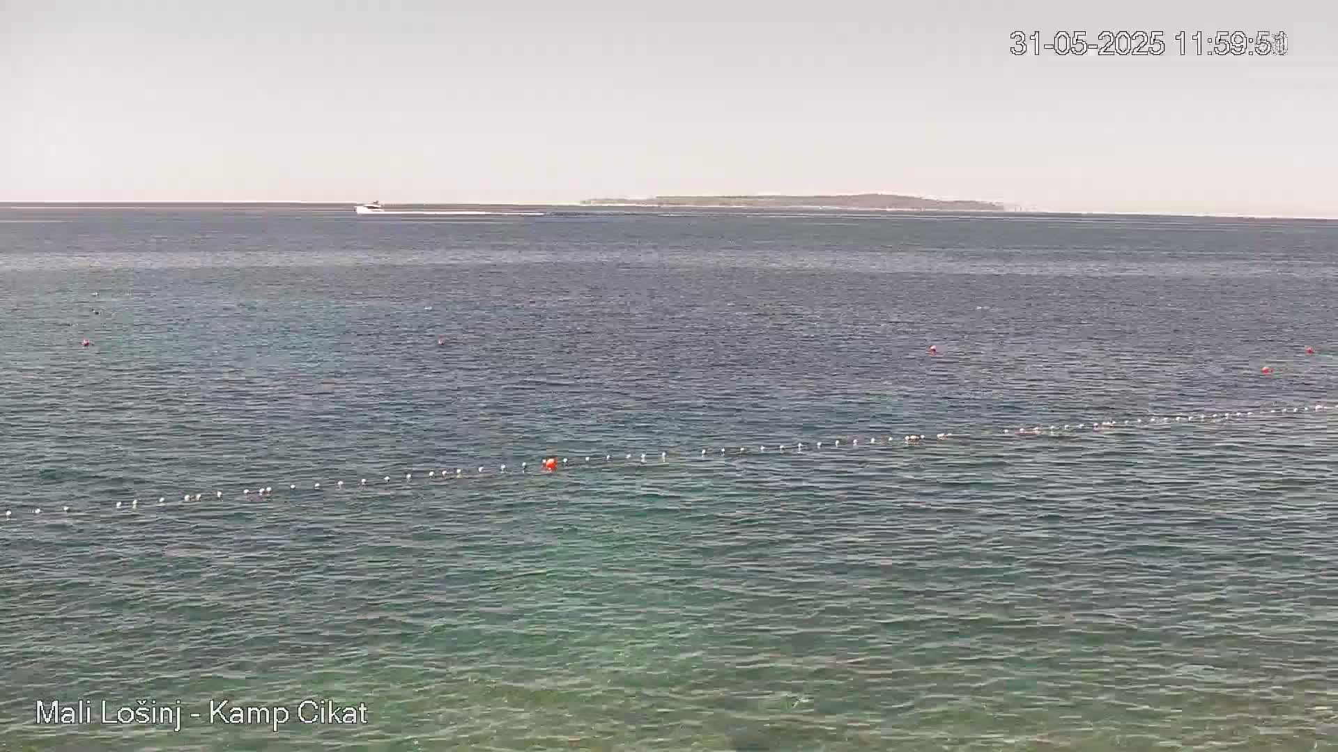 A calm, sunny day shows a view of a clear body of water with a distant shoreline and a swimming area marked by buoys.