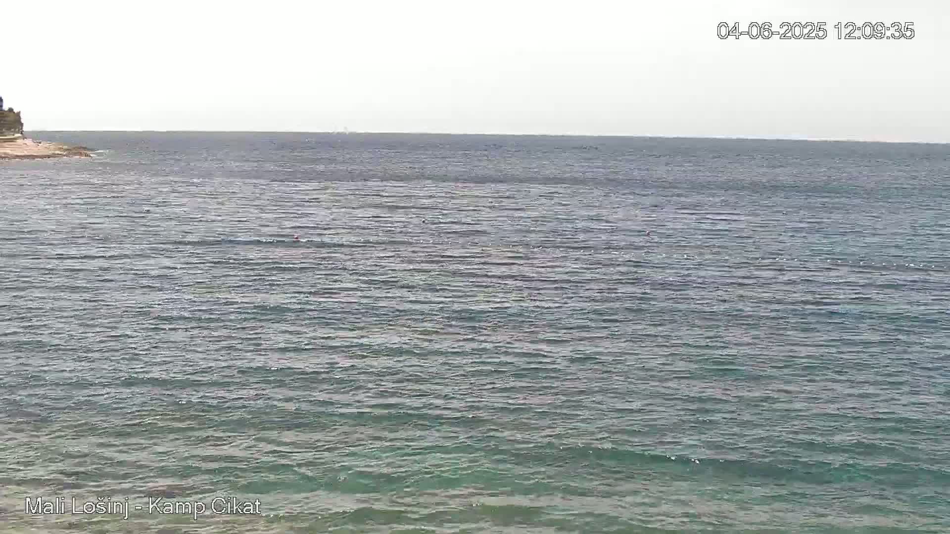 A mostly calm, gray-green sea stretches to the horizon under an overcast sky, with a small rocky outcrop visible in the distance to the left.