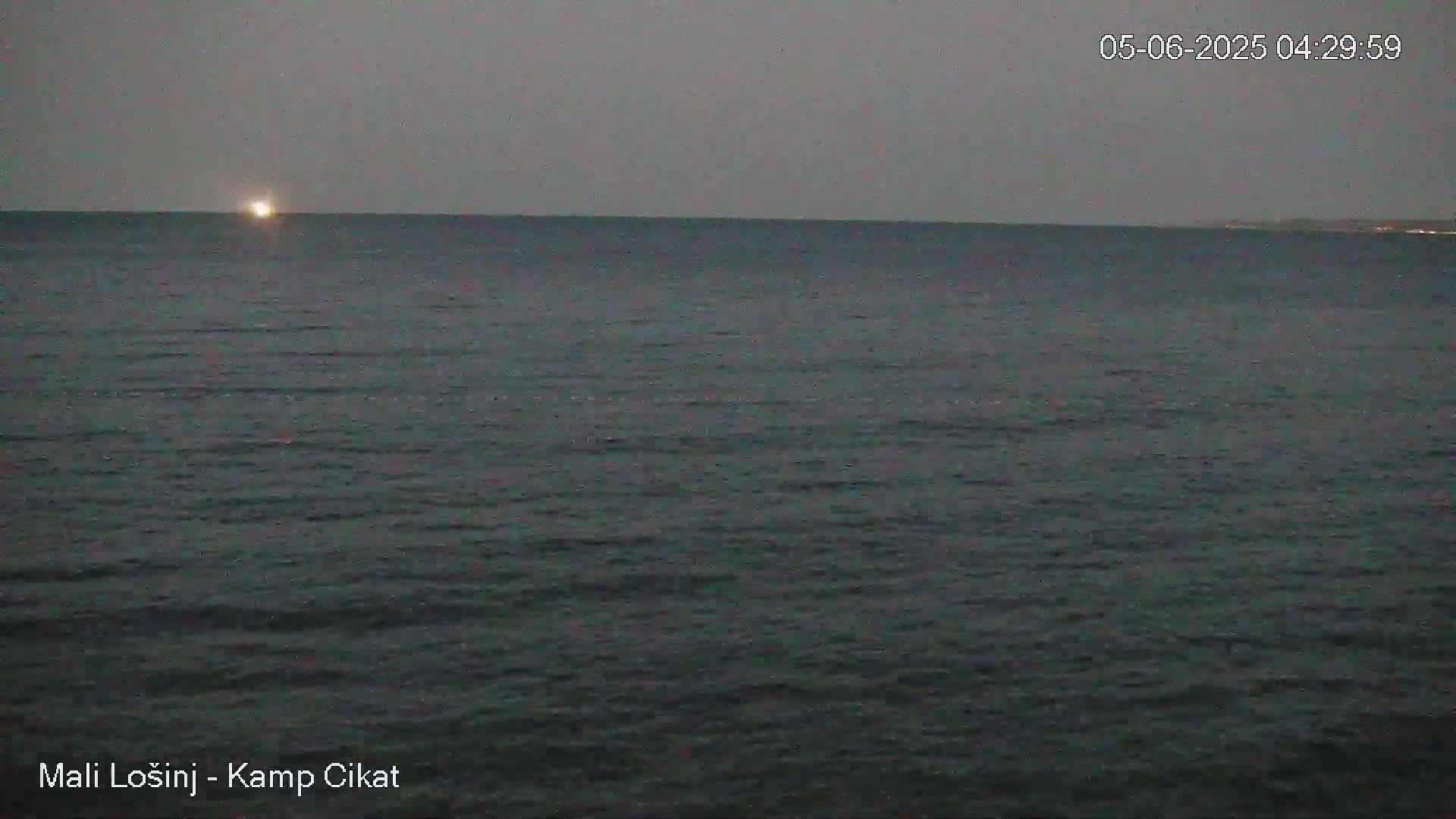 A calm, dark-grey sea is visible under an overcast sky, with a faint light appearing on the horizon.
