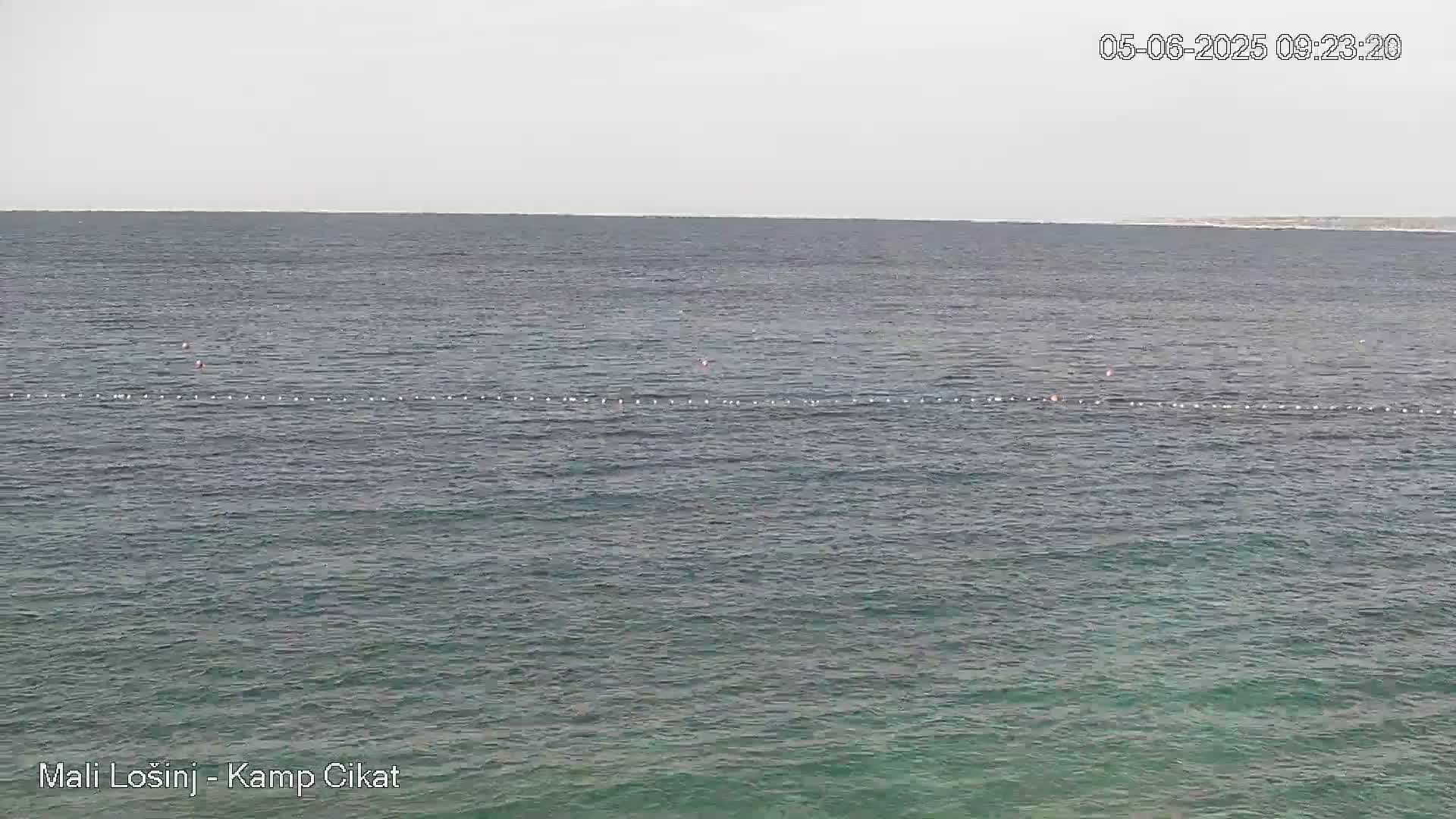 A calm, gray day shows a body of water with a line of buoys in the middle distance.