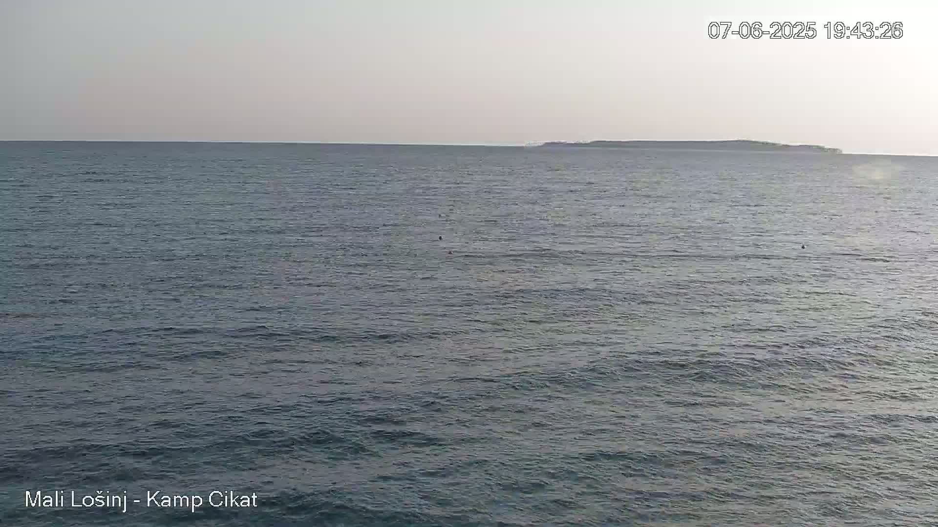 A calm, gray sea stretches to a distant, low-lying island under a pale sky.