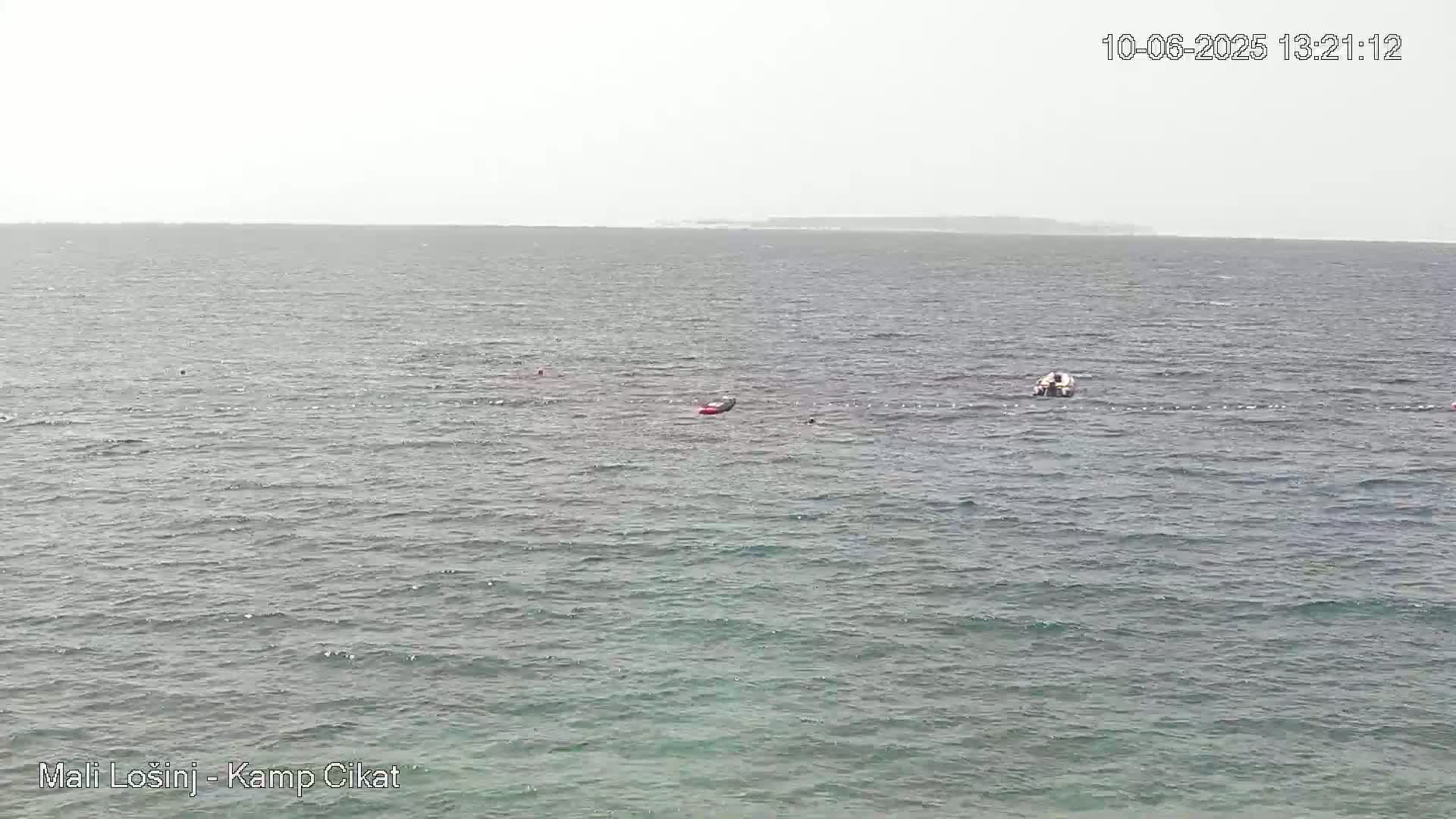 A hazy, overcast day shows a calm sea with a small boat and inflatable raft visible, and a distant shoreline.