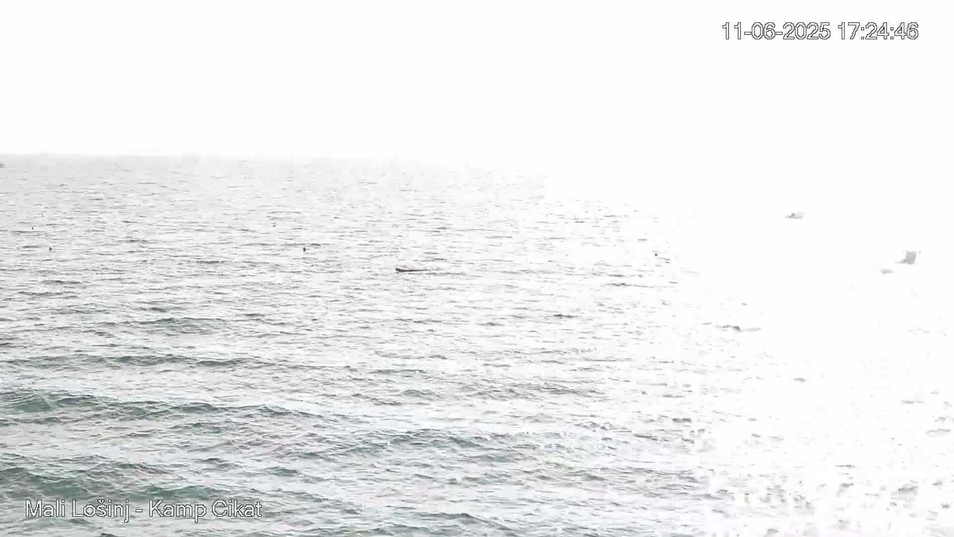 A mostly overcast sky overlooks a calm sea with a few small boats visible in the distance.