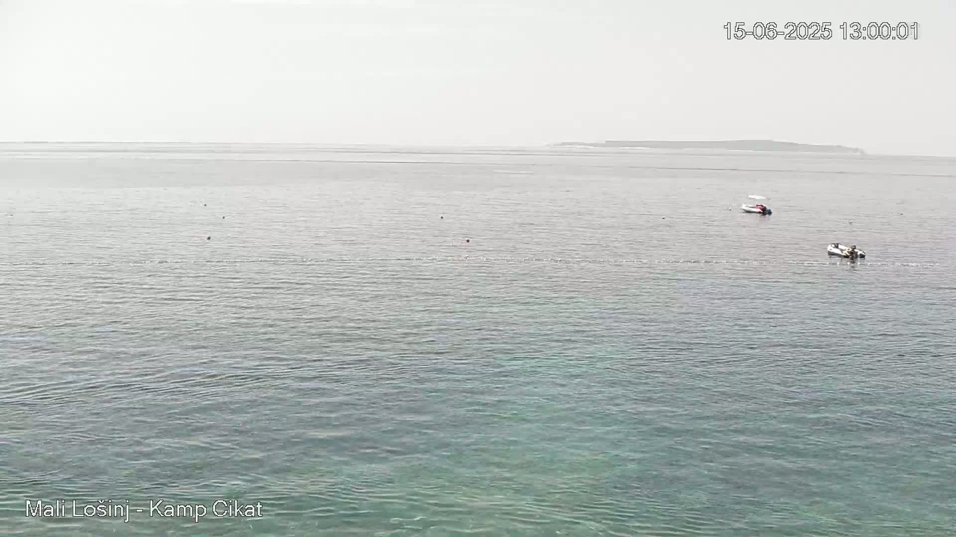 A hazy, calm sea with two small boats and a distant landmass visible on the horizon.