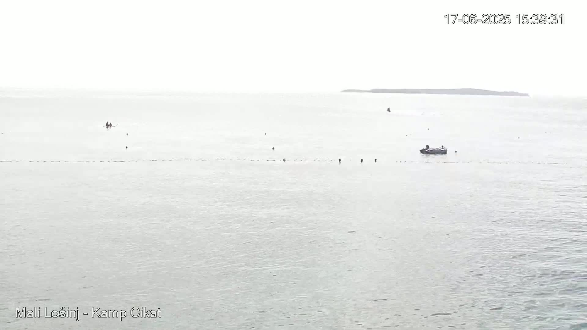 A calm, overcast day shows a wide expanse of light gray water with a few small boats and a distant landmass.