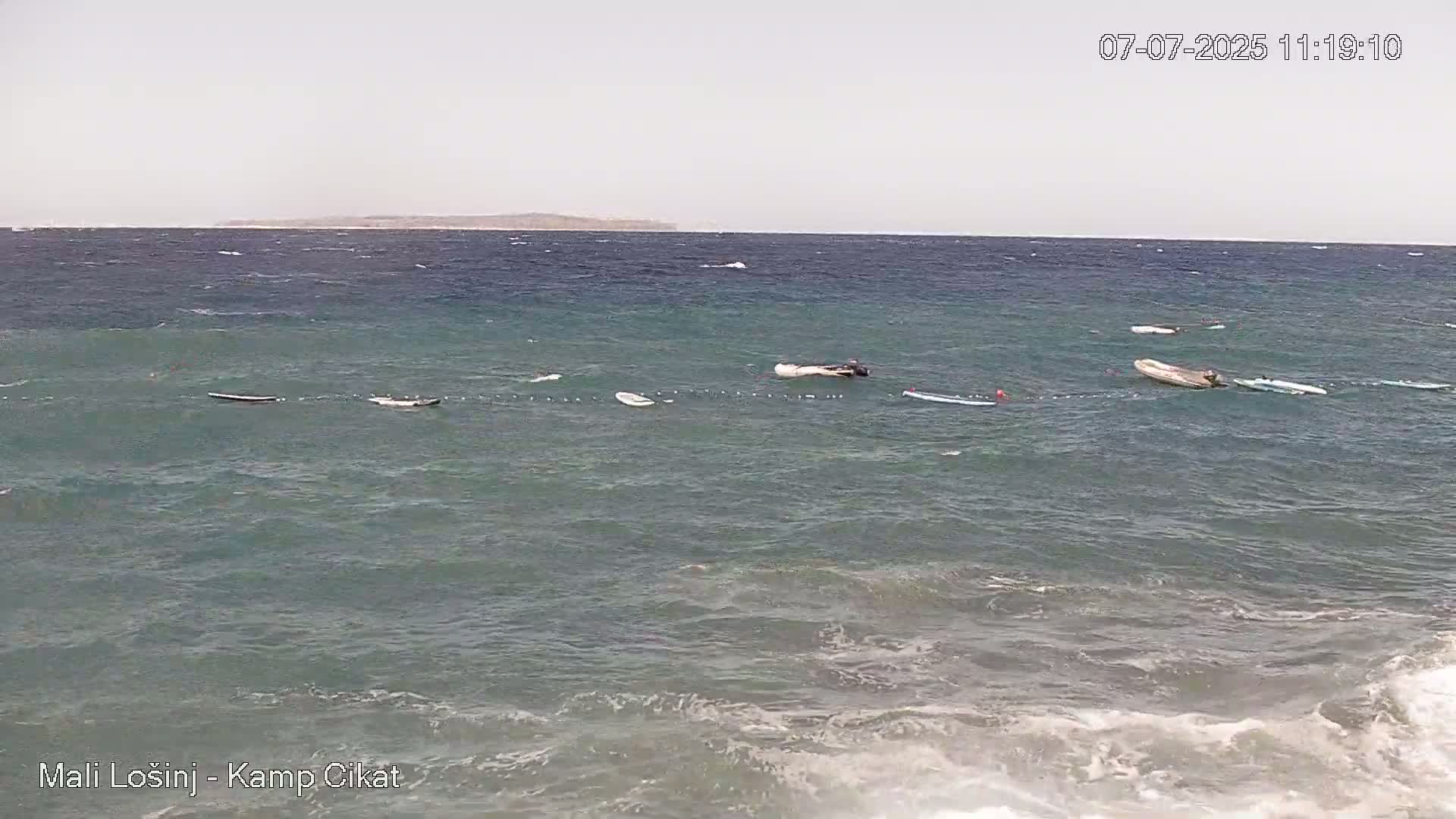 Several paddleboards and small boats float on a somewhat choppy sea under a cloudy sky.