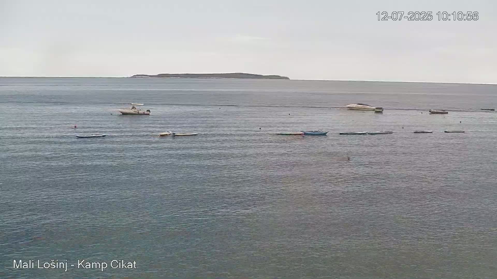 Several small boats and a larger motorboat are scattered across a calm, gray sea with a distant island visible on the horizon under an overcast sky.