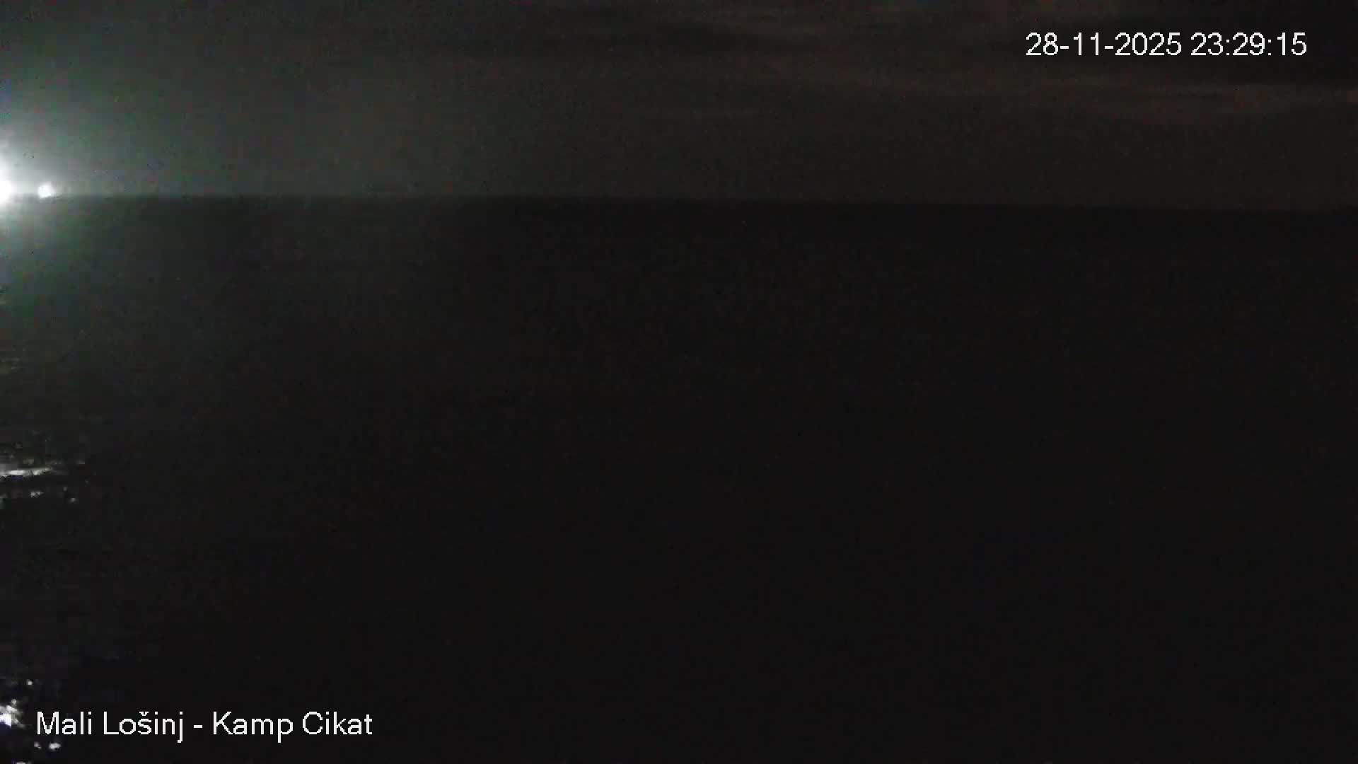 A dark, nighttime scene shows a body of water with a bright light source emanating from the far left, all under clear skies.