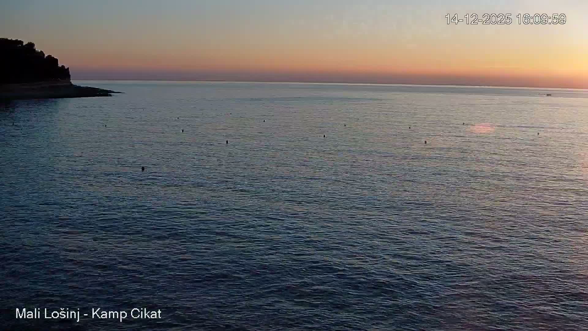 A wide view captures a grey, choppy sea under a heavily overcast sky, with a dark, tree-covered coastline on the left and several small objects floating in the water.