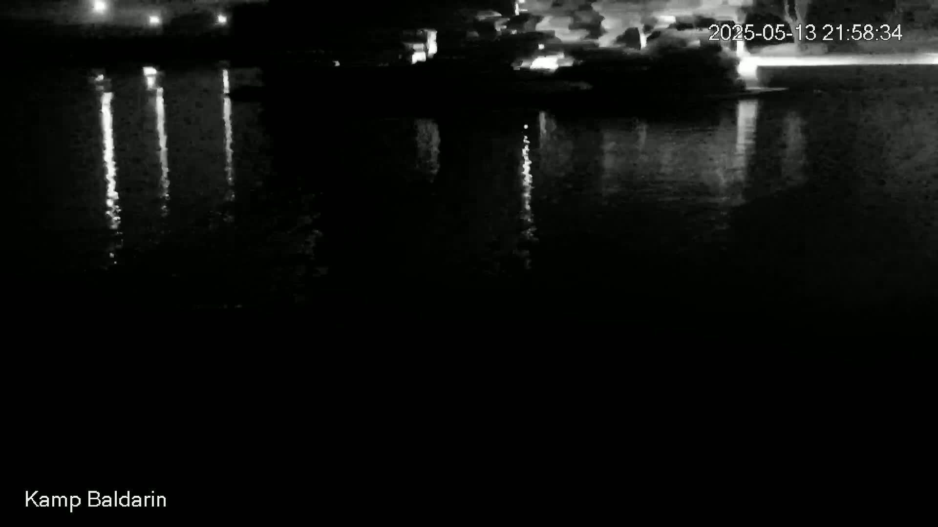 The image shows the dark reflection of lights on a calm body of water at night.
