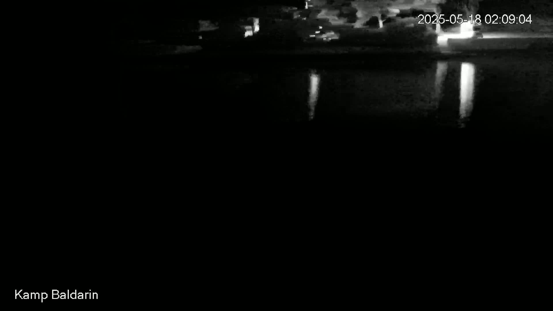 A nighttime, low-light image shows a dark body of water reflecting lights from a distant shoreline.