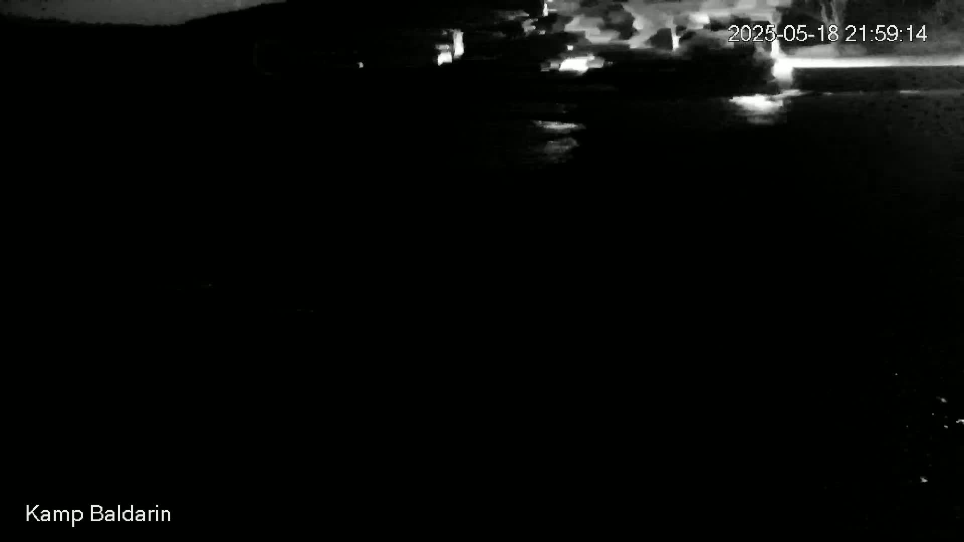 A dark, nighttime scene shows a body of water reflecting a bright, cloudy sky.