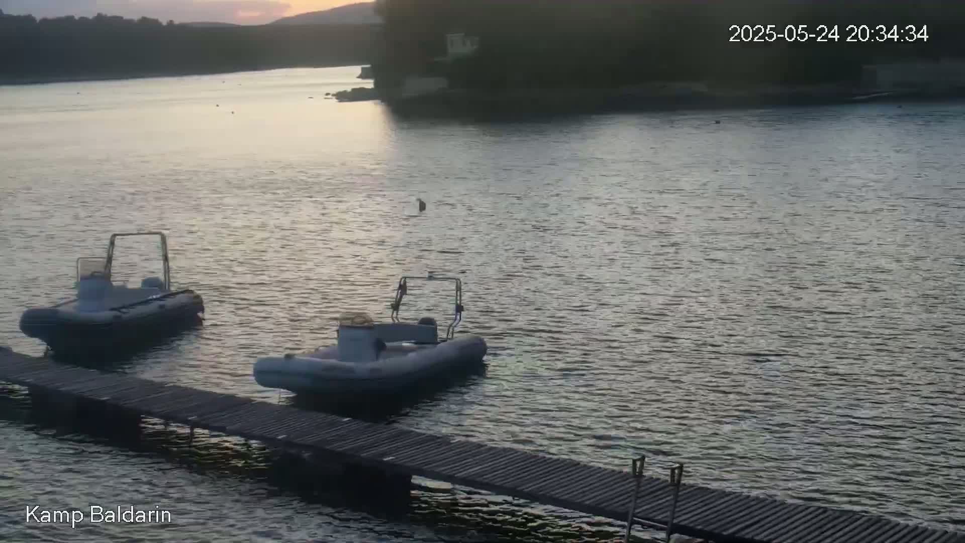 Two small motorboats are moored at a wooden dock on calm water at sunset.