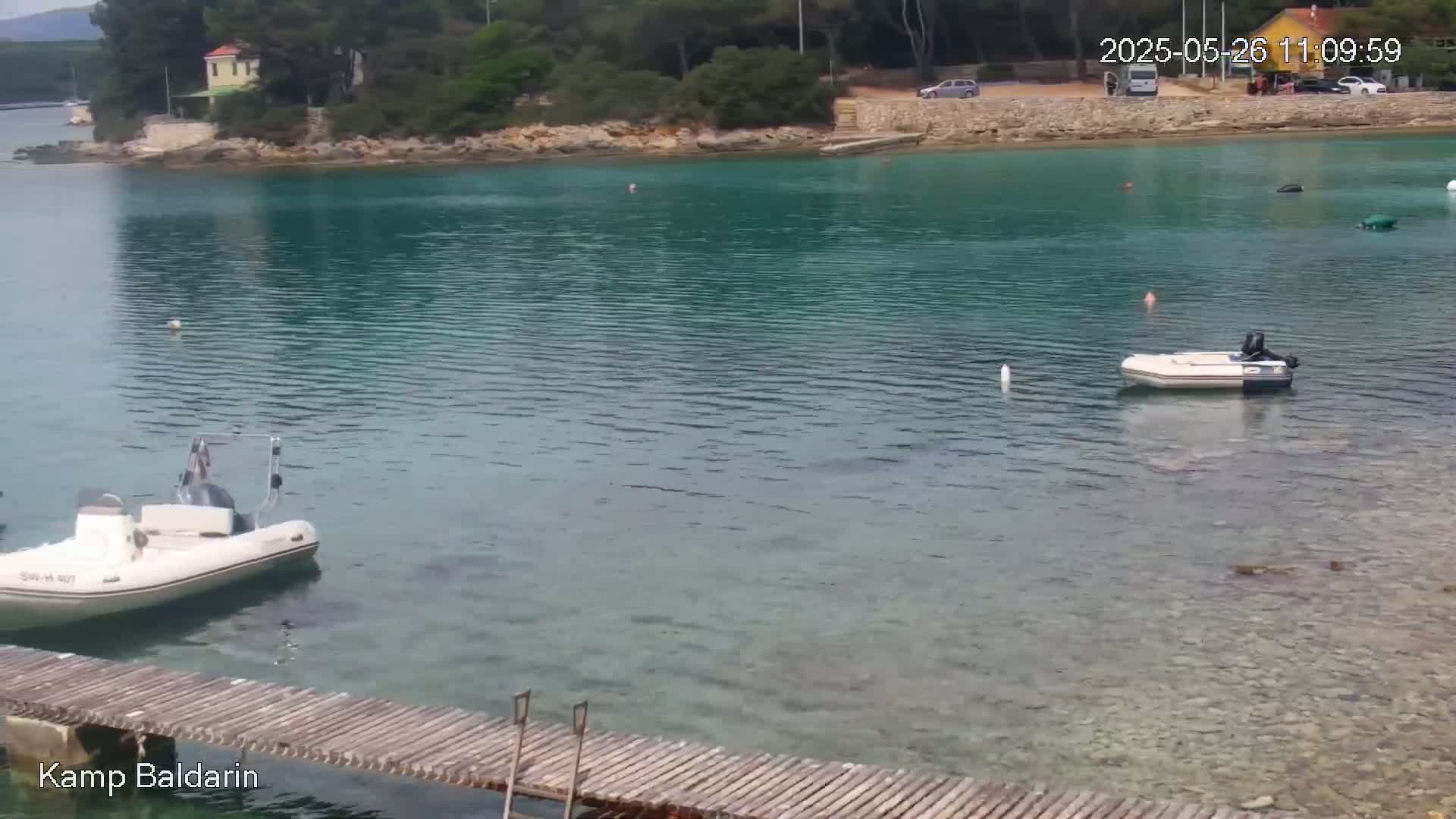 A calm, clear turquoise bay with several small motorboats and a wooden dock, surrounded by green trees and a small building on a rocky shore.