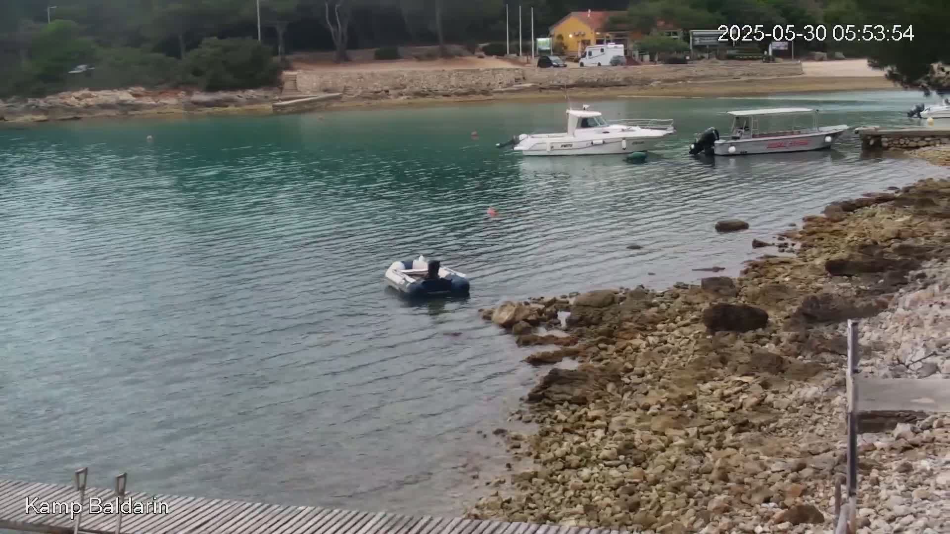 A calm, teal-colored bay with several boats moored near a rocky shore.