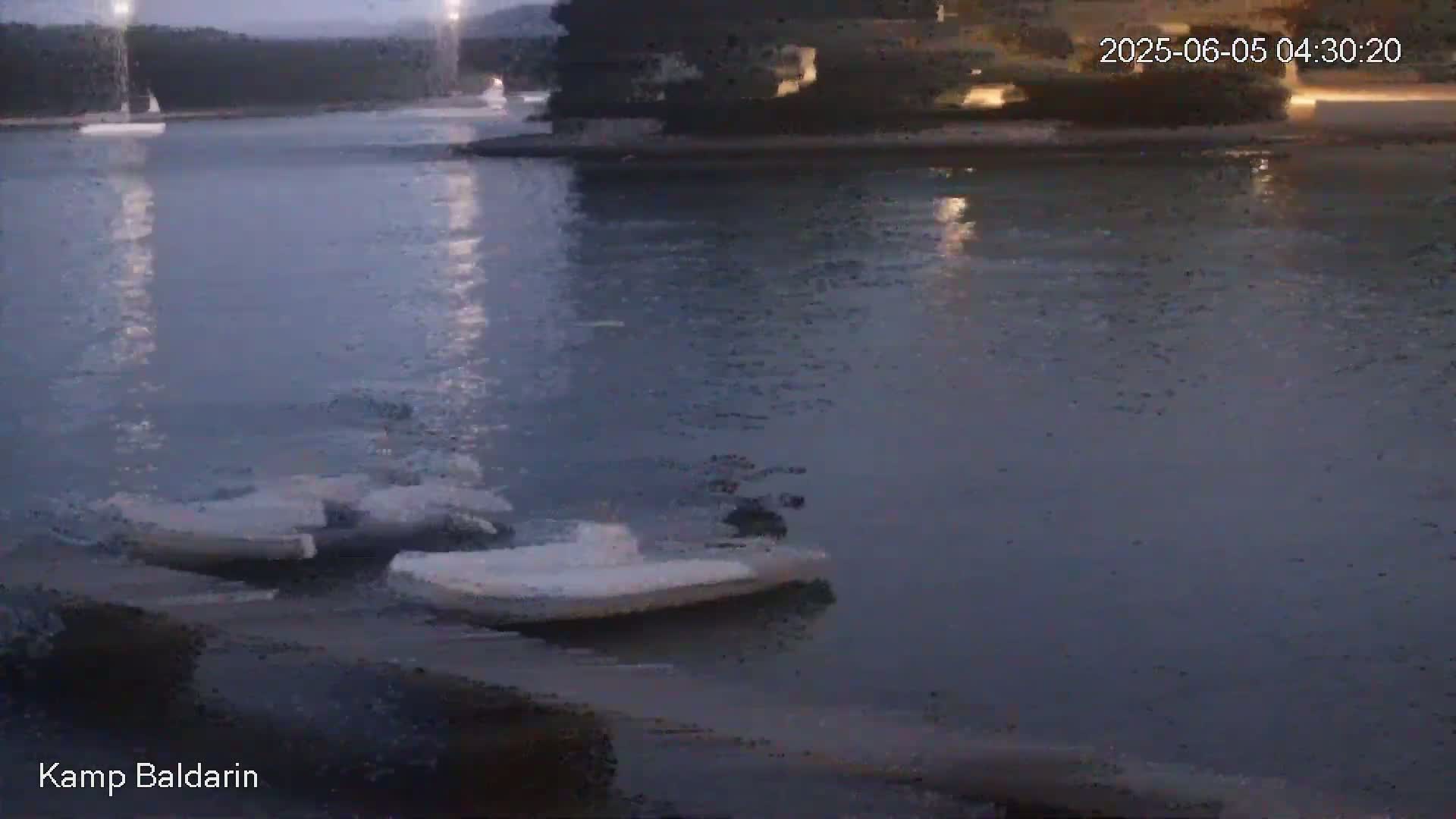 Several small boats are moored near a dark shoreline on a calm, twilight body of water.