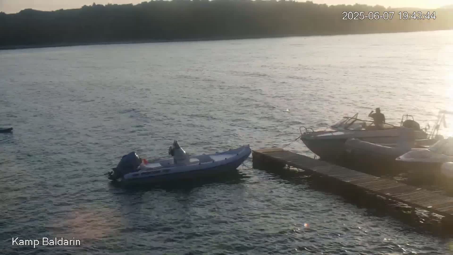 Two motorboats are moored at a wooden dock on calm water under a sunset sky.