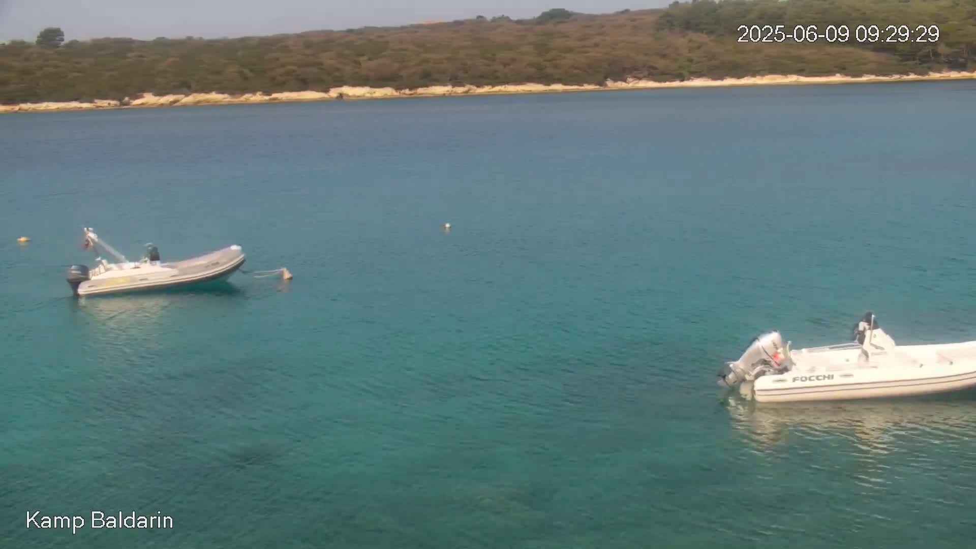 Two inflatable boats are moored in a calm, clear turquoise bay, with a verdant hillside visible in the background.