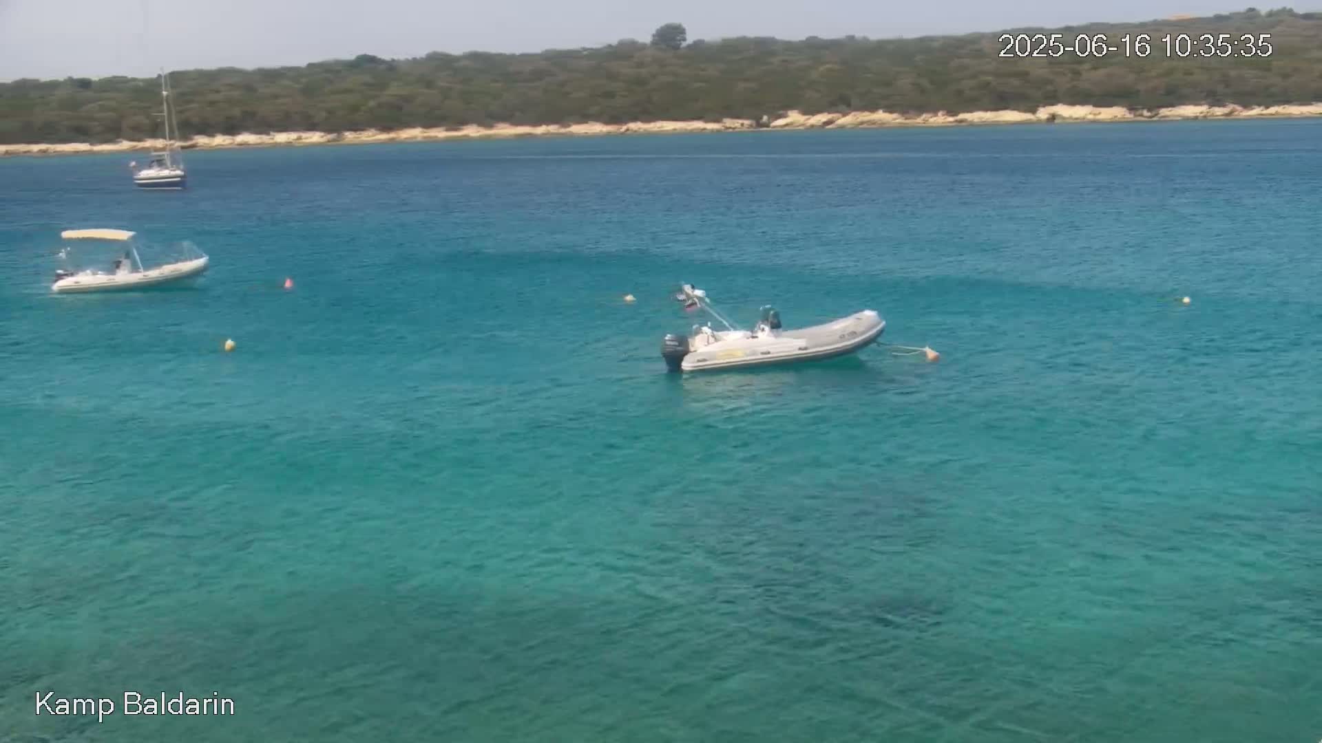 Three small boats are in a calm, clear turquoise sea near a green, tree-covered shoreline under a mostly sunny sky.