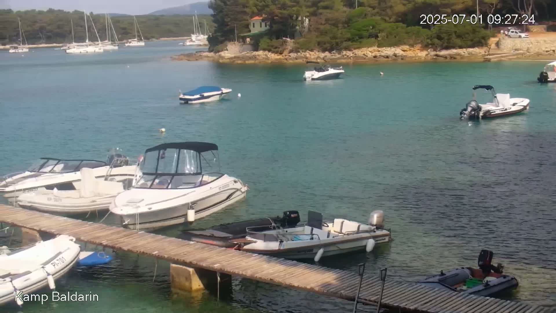 Several motorboats and sailboats are moored in a calm, clear turquoise bay, surrounded by green vegetation and a small island.