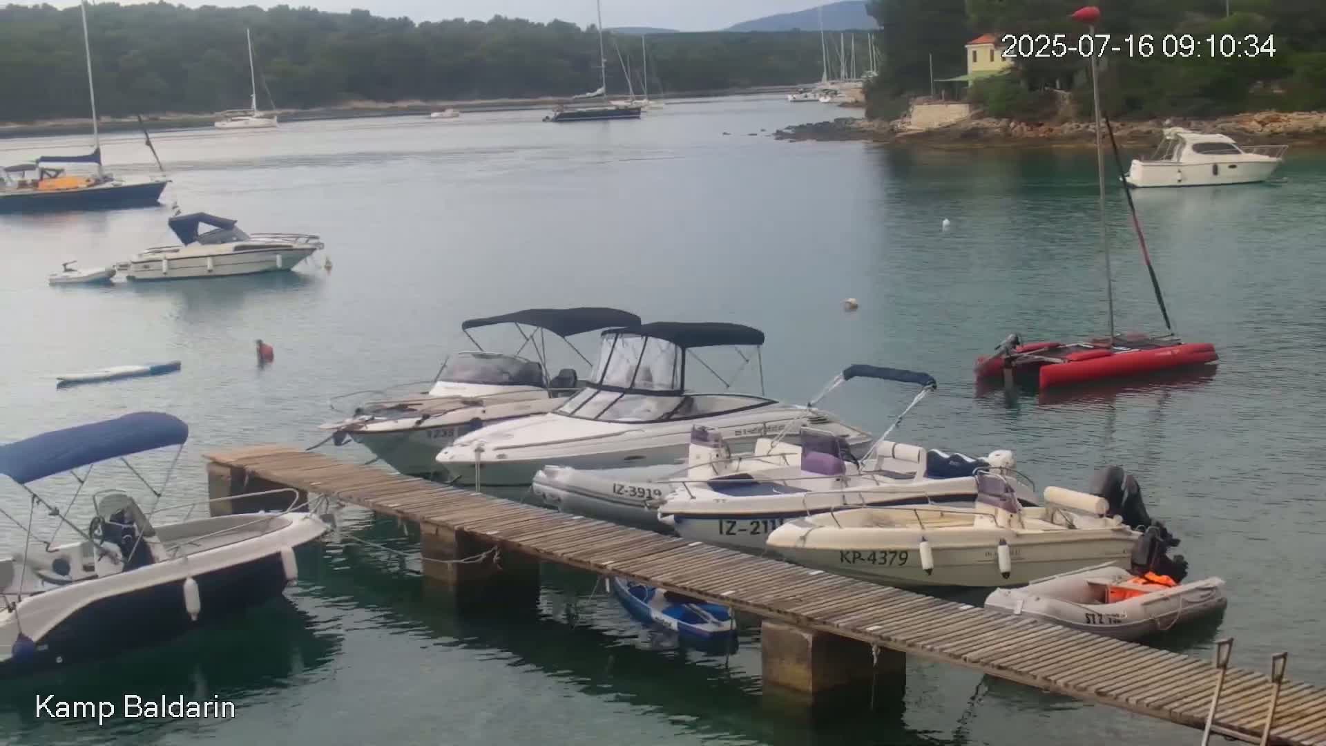 Several motorboats are docked at a wooden pier in a calm, clear bay, with additional boats anchored nearby.