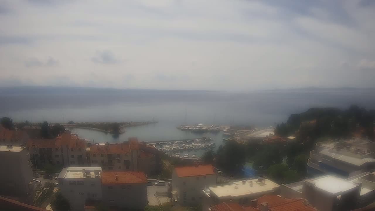 An aerial view shows a hazy, overcast day over a coastal town with a marina filled with boats.