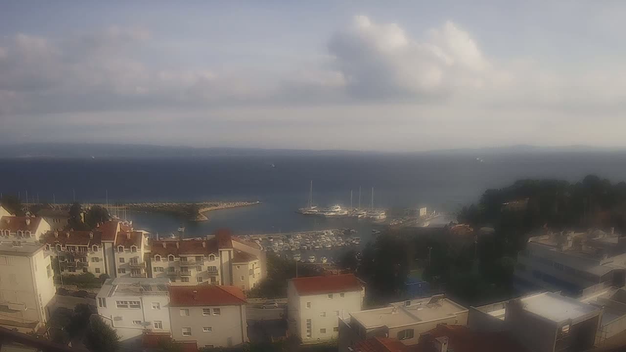 A partly cloudy day overlooks a harbor filled with boats and a coastal town of low-rise buildings.