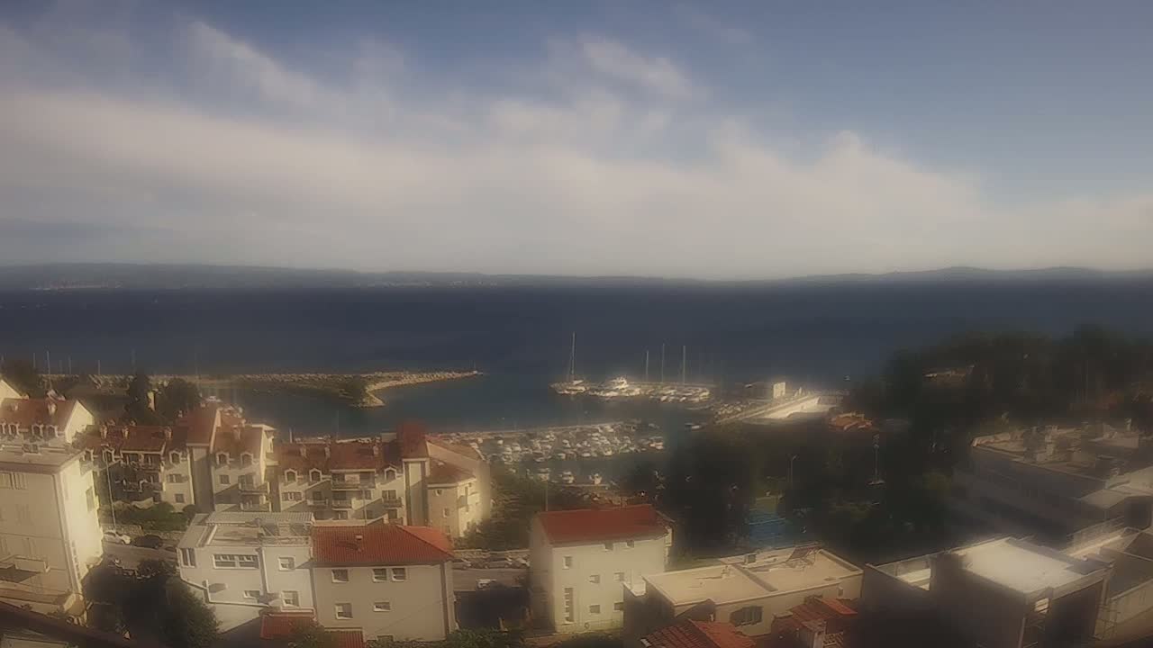 A coastal town with low-rise buildings overlooks a calm body of water containing a marina under a partly cloudy sky.