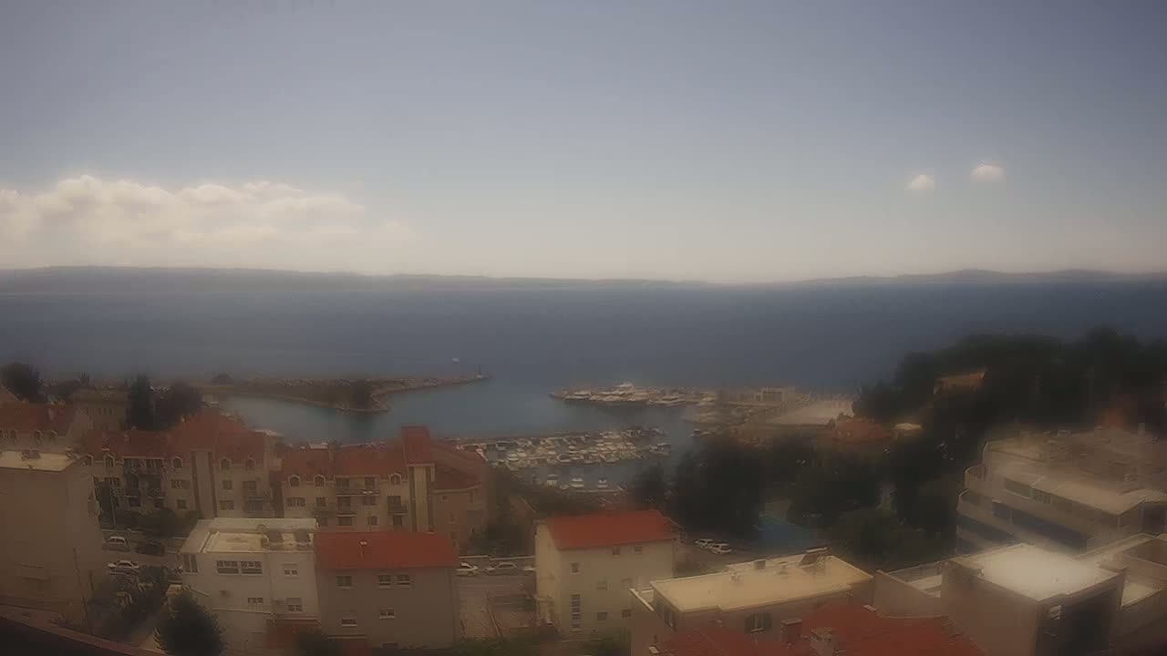 A hazy, partly cloudy day overlooks a marina filled with boats and a coastal town with multi-story buildings.