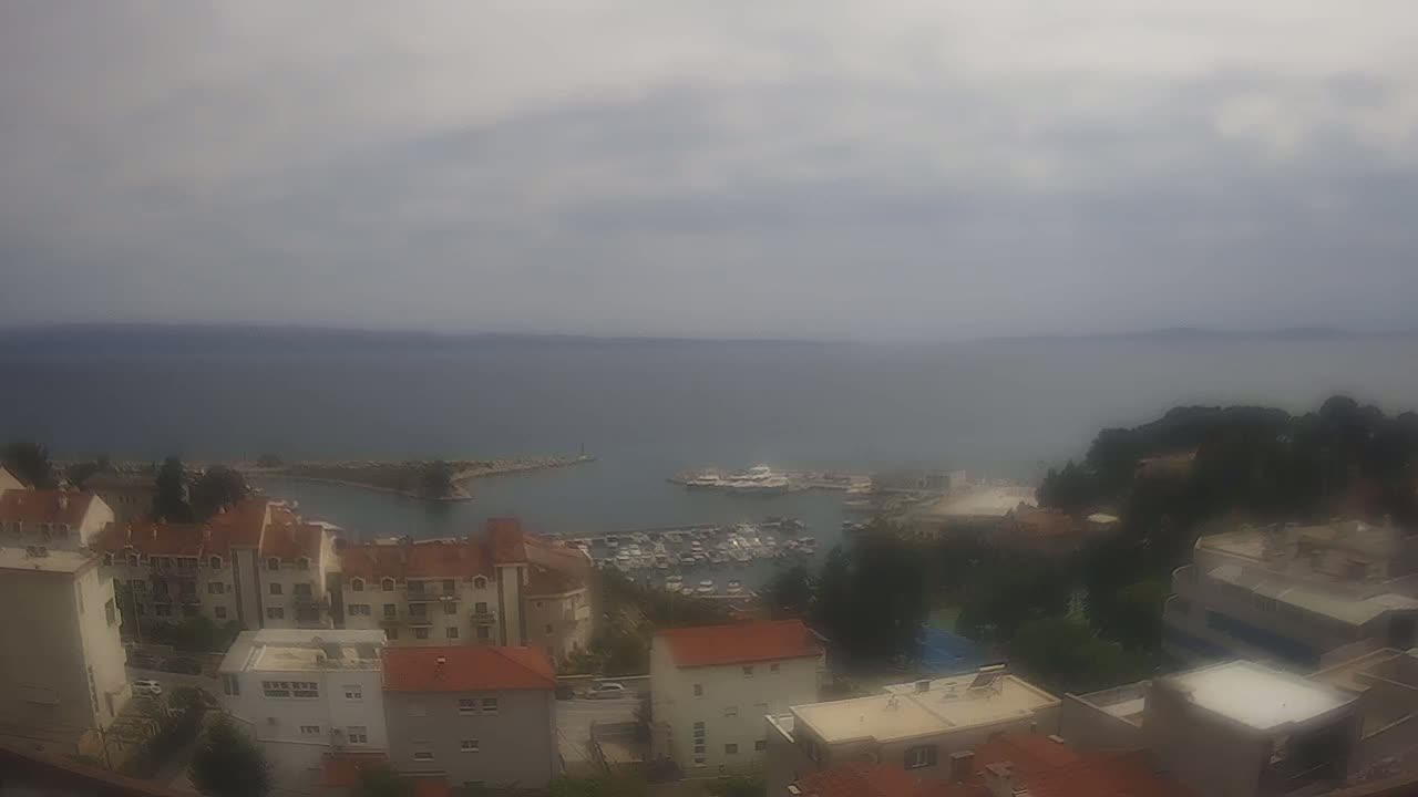 A hazy view of a coastal town with a harbor filled with boats, under an overcast sky.