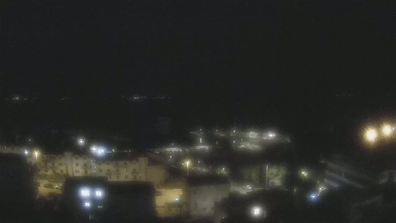 A nighttime, high-angle view of a residential area with dimly lit buildings and parking lots under a dark sky.