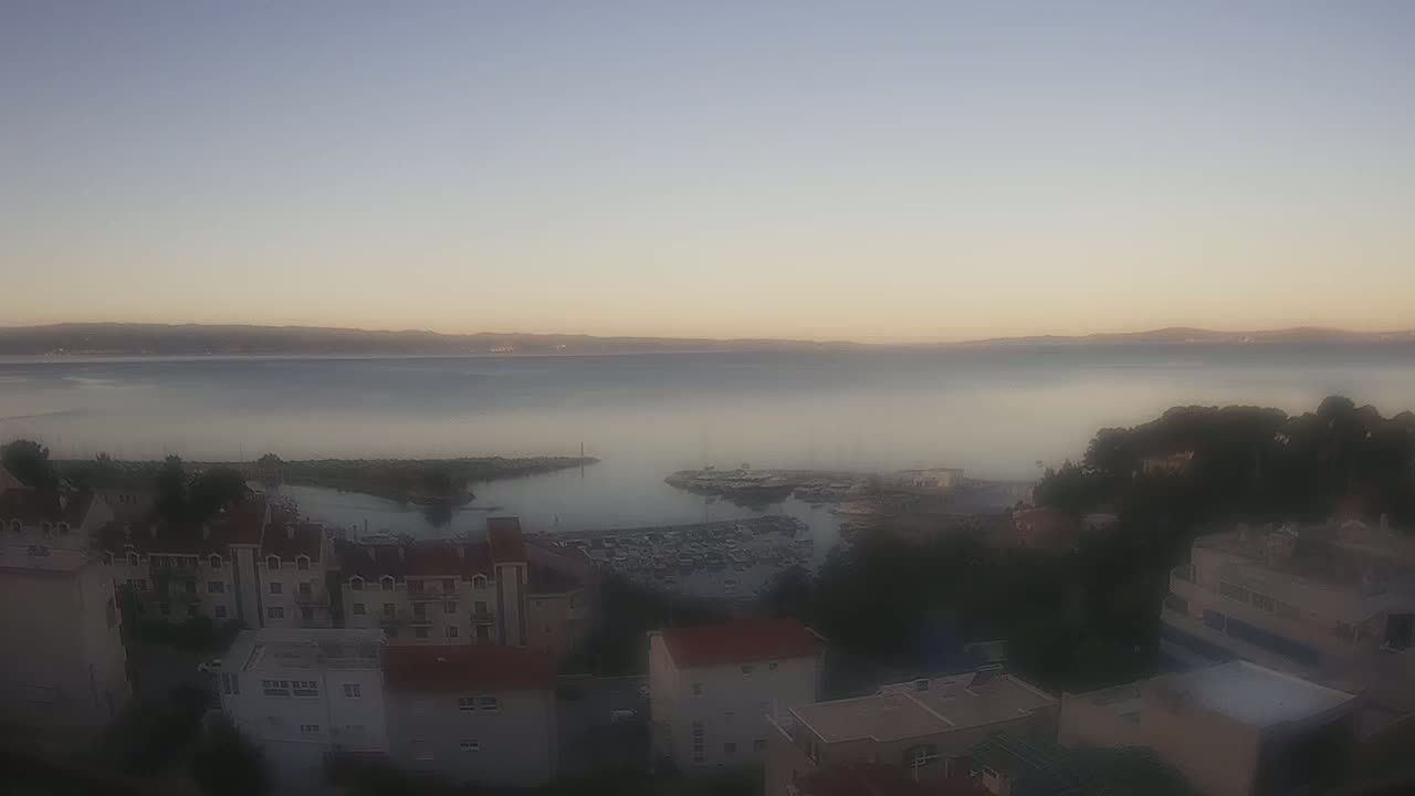 A hazy sunrise over a calm body of water with a marina and residential buildings visible in the foreground.