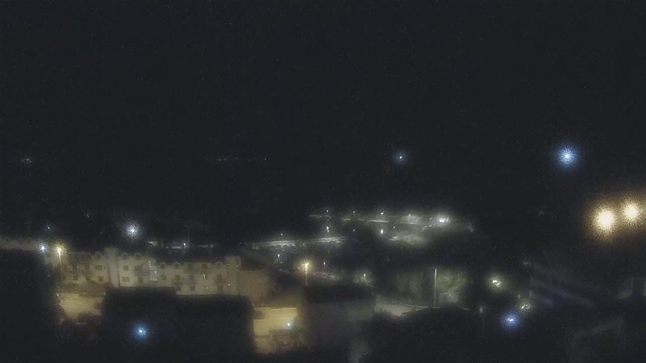 A nighttime, high-angle view shows a dimly lit residential area with buildings and streetlights under a dark sky.