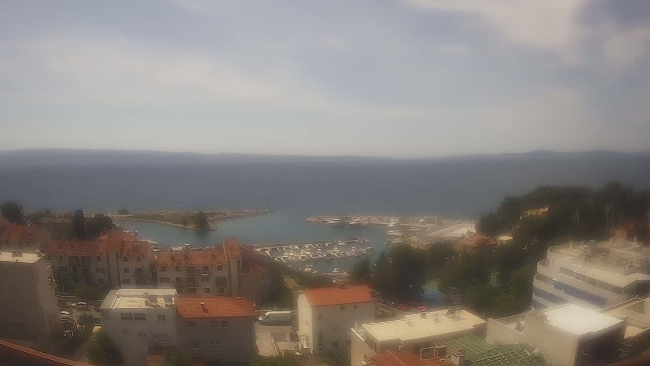 A hazy, sunny day overlooks a coastal town with a marina filled with boats, and buildings with red-tiled roofs.