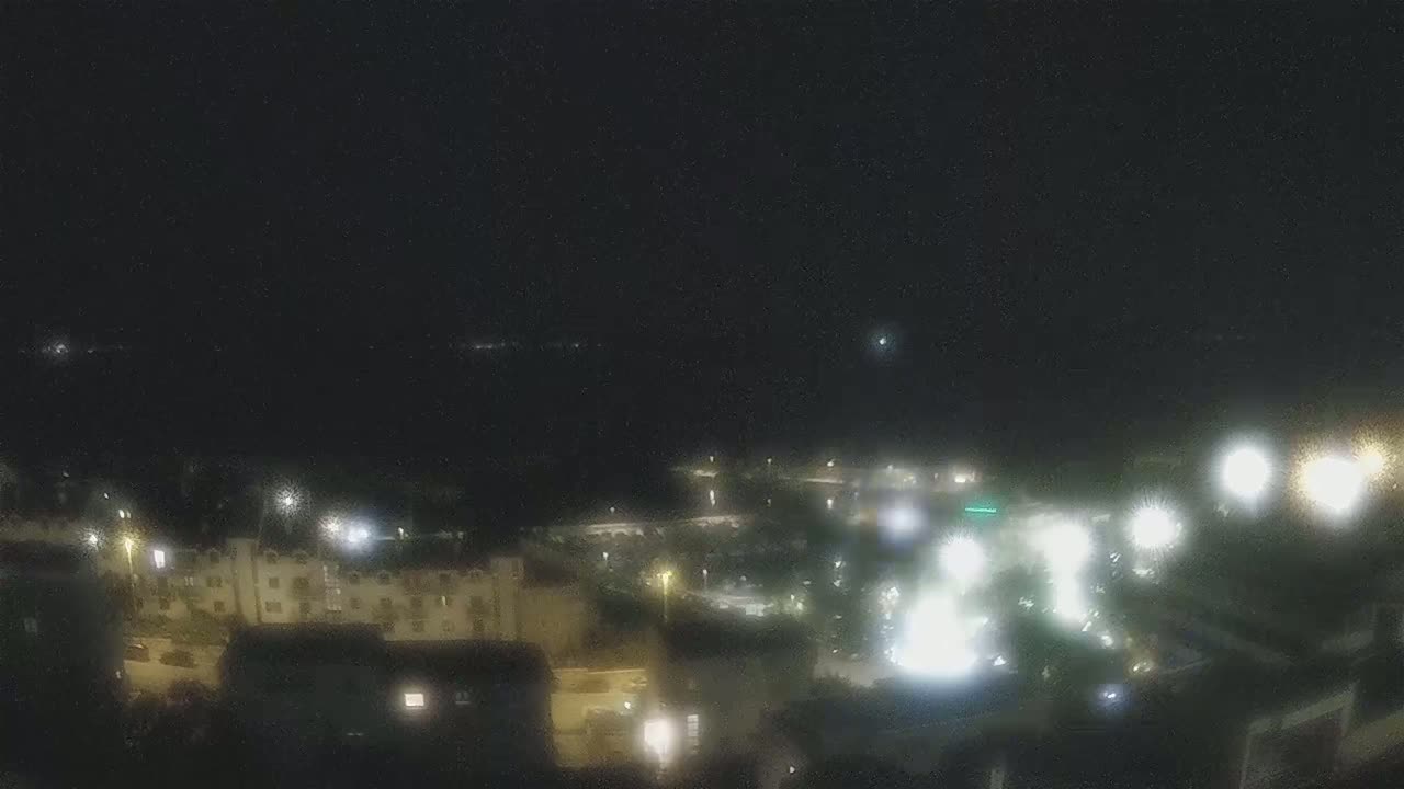 A nighttime, high-angle view shows a coastal town with buildings and streetlights illuminated against a dark sky.