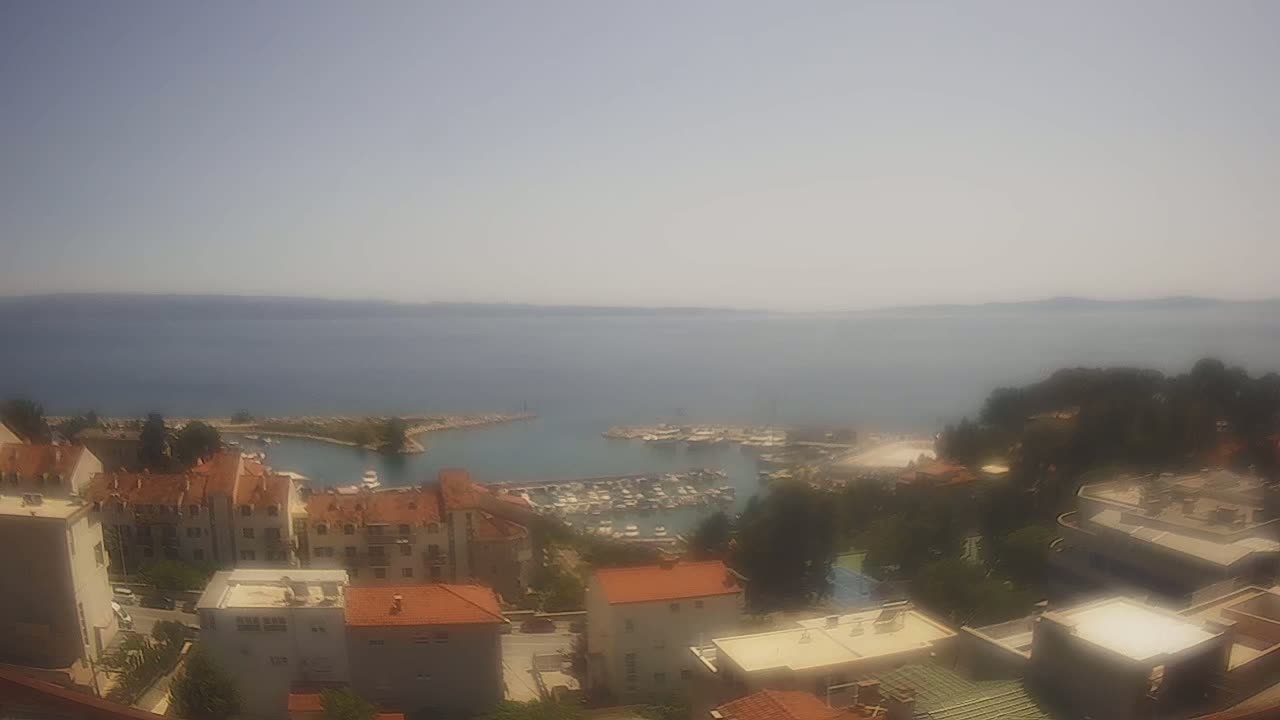 A hazy, sunny day overlooks a small marina filled with boats, nestled between a town of low-rise buildings and a calm sea.