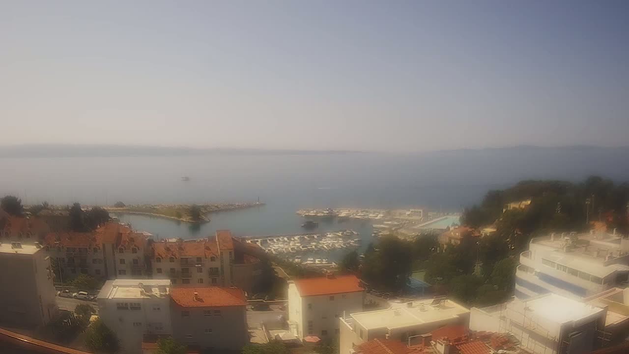 A hazy, sunny day overlooking a calm sea with a marina filled with boats and a collection of buildings on a hillside.
