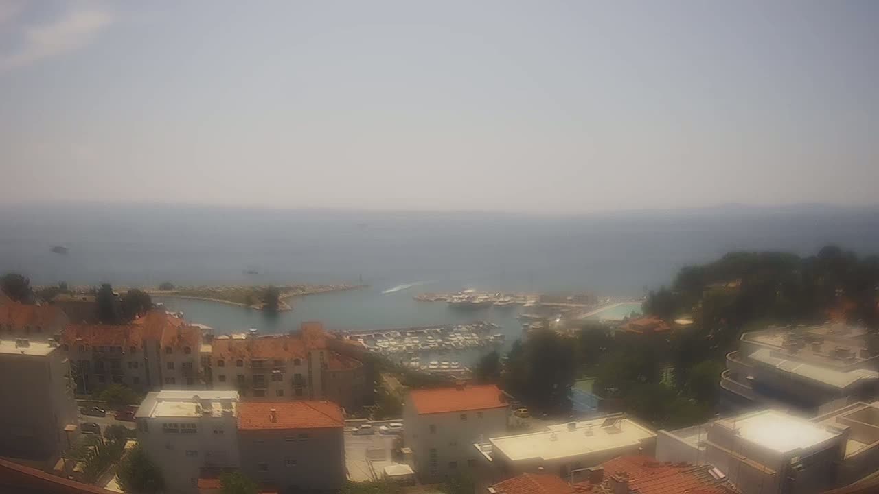A hazy, sunny day overlooks a coastal town with a marina filled with boats, surrounded by low-rise buildings.