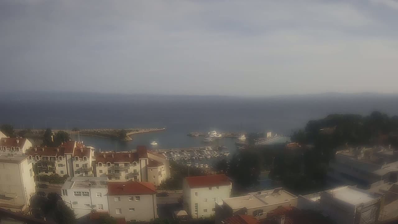A hazy, overcast day reveals a coastal town overlooking a calm sea with a marina filled with boats.