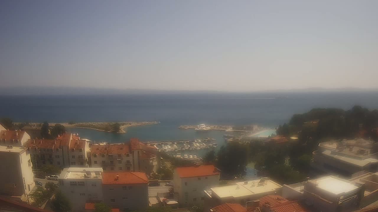 A hazy, sunny day overlooking a calm sea with a marina filled with boats, and a collection of low-rise buildings on a hillside.