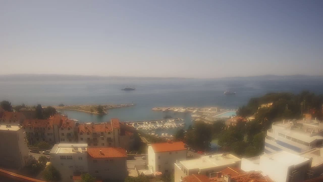 A hazy, sunny day overlooking a marina filled with boats, nestled between buildings and a calm blue sea.