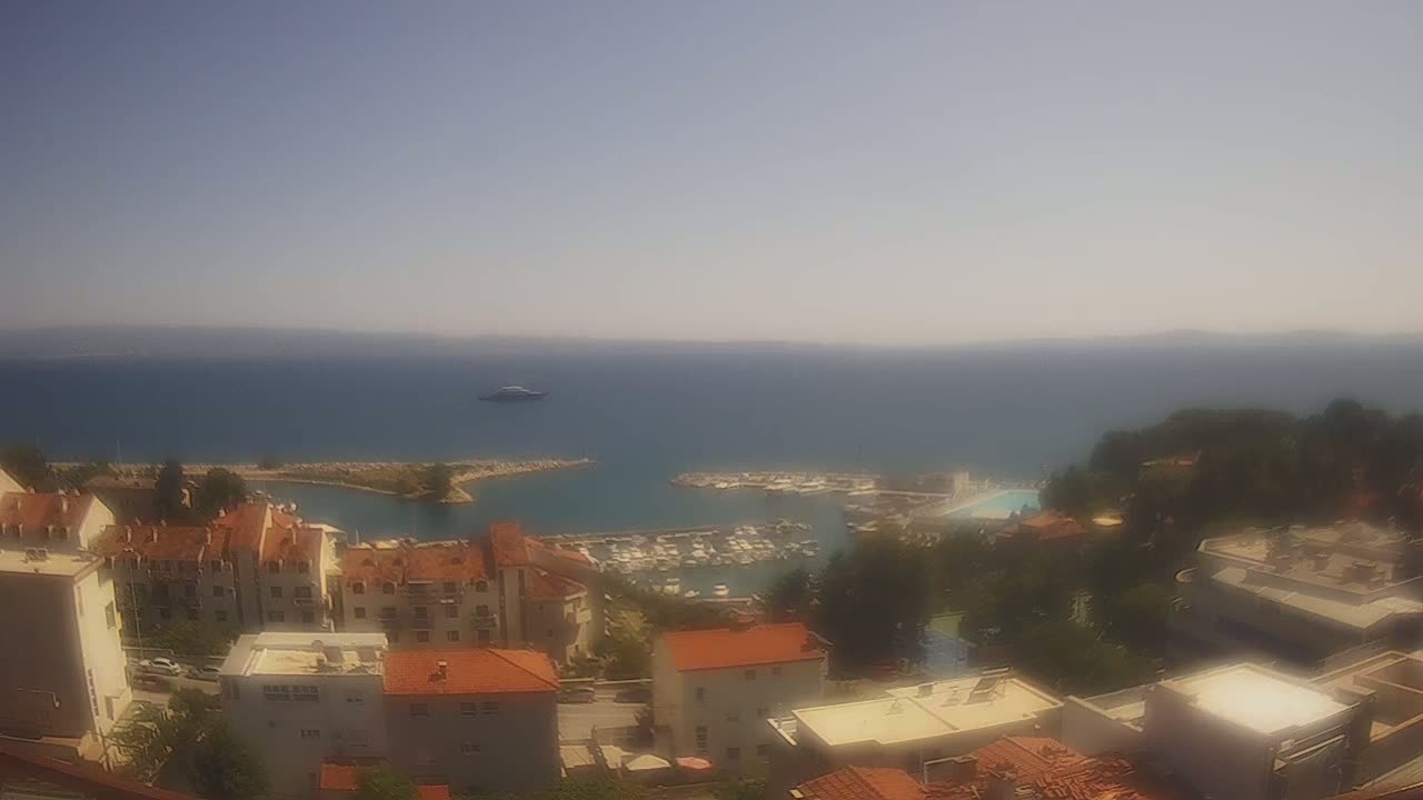 A hazy, sunny day overlooking a coastal town with a marina filled with boats, and the calm blue sea stretching to the horizon.