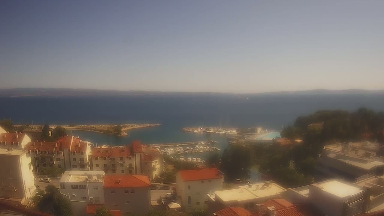A hazy, partly cloudy day overlooks a coastal town with a marina filled with boats, and the ocean stretches to distant hills.