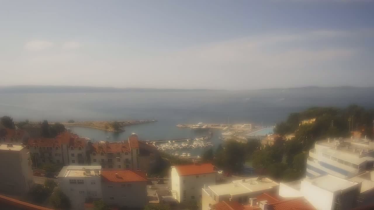 A hazy view overlooking a coastal town with a marina filled with boats, under a mostly clear sky.