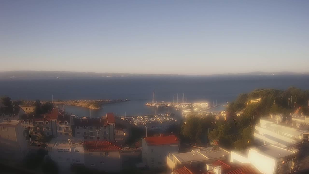 A hazy view overlooking a coastal town with a marina filled with boats, under a mostly clear sky.